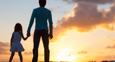 An adult and child standing in front of a sunset